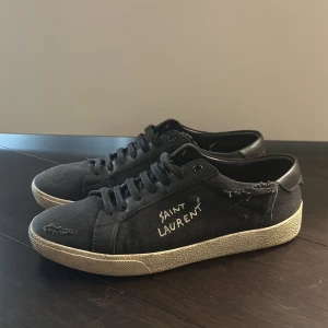 Sneakers från Saint Laurent ord pris: 7000kr - Ett par svarta sneakers från Saint Laurent med vit sula och snörning. Skorna har en sliten look med fransiga detaljer och Saint Laurent-logotypen broderad på sidan. Nypris 7000kr