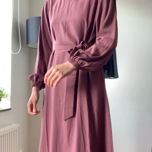 Rosa Abaya / Modest Klänning - Säljer abaya då jag är för lång för den. Nyttskick och kommer med matchande bälte. Fint ogenomskinligt material, har osynlig dragkedja i nacken och fickor! Behöver bara strykas. Längd är 133cm. Jag är ca 173cm lång för referens🩷Köpt för 500