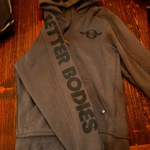 Better Bodies PRO hoodie - Gunmetal grey, svart tryck / brodyr i storlek XL, oanvänd. 