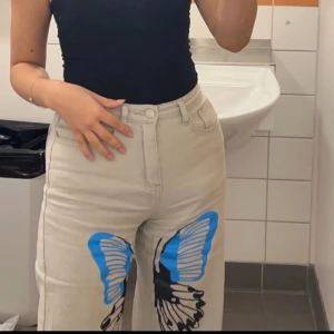 Jeans med tryck - Ett par grå/beige jeans med svart, blå tryck på en fjäril 