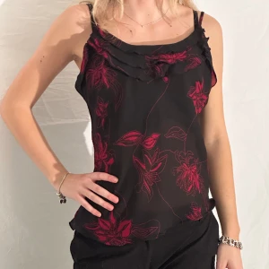 linne med volang - svart linne med röda detaljer i tunt och styvt material. Volangdetaljer vid bysten och en snedskuren kant. Justerbara smala axelband.  tjejen på bilden har i vanliga fall xs-s