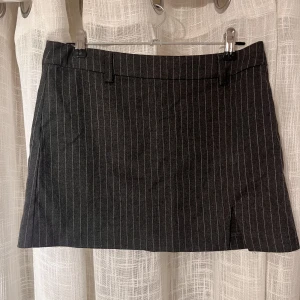 Kjol ginatricot - Mörkgrå, randig minikjol från ginatricot. Storlek XS. Har en liten slits framtill samt stängs med dragkedja vid sidan. Aldrig använd då den inte  passar mig som föredrar högmidjade kjolar (kjolen är snarare low-midwaist).😊 Använd gärna köp nu-funktionen🥰