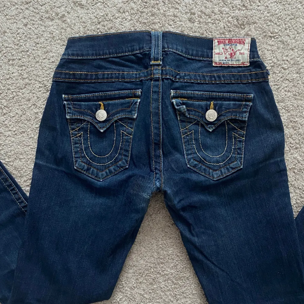 Ett par jättefina mörkblåa och utsvängda true religion jeans i storlek 28. De är lite slitna på ett par ställen med det är inget som syns särkilt mycket. Midjemåttet är 35 cm (tvärs över) och innerbenslängden är ca 74 cm. Skriv för fler frågor! . Jeans & Byxor.