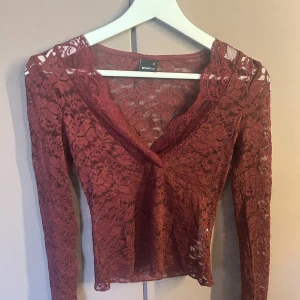 Vinröd spetsblus från Gina Tricot - Supersnygg vinröd spetsblus från Gina Tricot med lång ärm och v-ringad hals. Blusen är helt i genombruten spets med blommigt mönster och har en figurnära passform. Perfekt för dig som vill sticka ut med en romantisk och trendig look.