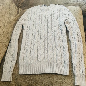 Ljusgrå kabelstickad tröja Lager 157 - Säljer en ljusgrå kabelstickad tröja från Lager 157 i storlek S. Tröjan har ett klassiskt flätmönster, rund hals och ribbade muddar vid ärmslut och nederkant. Perfekt för dig som gillar stilrena och mysiga plagg med lite preppy känsla.