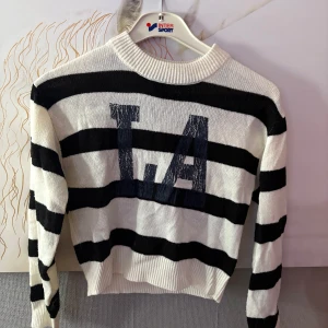 Randig stickad tröja från H&M Divided - Snygg stickad tröja från H&M Divided i svart och vitt med breda ränder och trycket 'L.A' framtill. Tröjan har lång ärm, ribbad halsringning och muddar. Perfekt för dig som gillar streetstyle och vill ha en chill vibe.