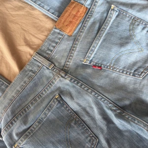 Levis 505 Bootcut ljusblå jeans - Ljusblå Levis 505 jeans i bootcut-modell med klassiska fem fickor och råa, fransiga benslut. Jeansen har en avslappnad passform och är tillverkade i mjukt denim med snygga slitningar. Perfekta för en chill och avslappnad stil.