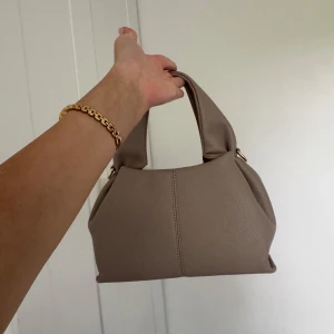 Beige toteväska  - Snygg beige handväska med mjuk, strukturerad form och breda handtag.  Perfekt storlek för att få plats med det viktigaste och passar till många olika outfits. Helt ny oanvänd.