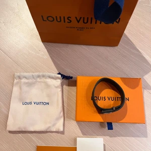 Louis Vuitton svart Monogram armband - Exklusivt svart armband från Louis Vuitton med klassiskt monogrammönster i mörkgrå toner. Snyggt och stilrent med silverfärgat spänne. Levereras med original ask och dustbag, perfekt för dig som gillar lyxiga accessoarer.