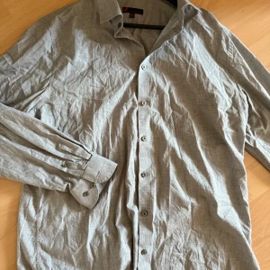 Grå skjorta med knappar - Snygg grå skjorta med klassisk krage, långa ärmar med dubbla knappar vid manschetten och diskret rutmönster i tyget. Tillverkad i mjuk bomull, perfekt för dig som gillar stilren och enkel look.(kommer strykas innan den skickas)