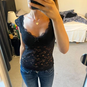 Svart spetsig blus med rosett😍 - Supersnygg svart blus i spets med v-ringning och liten rosett framtill. Toppen är figurnära och har korta ärmar i genombruten spets. 