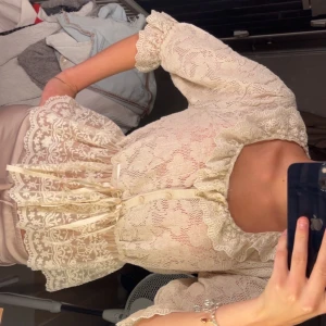  spetstopp med volang - Superfin topp i ljus beige med spets mönster och volangdetaljer vid hals och ärmslut. Koftan/topp har knappar framtill, markerad midja med knytband. Det står att tröjan är i storlek XL men jag har vanligtvis xs och jag tycker den sitter perfekt på mig får helt enkelt inte användning av den längre!