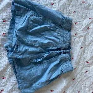 Blå shorts med snörning från H&M 146/152 - Snygga ljusblå shorts från H&M med bred resår i midjan och snörning framtill. De har två stora fickor på sidorna och är gjorda i mjukt bomullstyg som känns chill och luftigt. Perfekta för varma dagar och enkel att matcha med en t-shirt.
