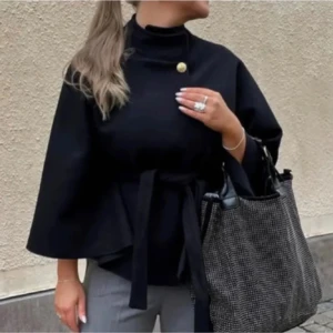 Missay kappa med bälte och knappdetalj - Stilren svart kappa med hög krage, knytband i midjan och en dekorativ guldig knapp vid halsen. Jackan har vida ärmar och en elegant, minimalistisk look som passar perfekt till höst och vinter. Enkel att matcha med både jeans och kostymbyxor. Som en poncho 