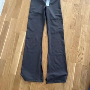Grå wide byxor från lager 157 strl S - Snygga grå byxor från lager 157 i storlek S med wide passform och slits vid benslut. Materialet är mjukt och har en lätt glansig finish, vilket ger en modern vibe. Perfekta för dig som gillar trendiga och bekväma byxor med lite extra attityd.