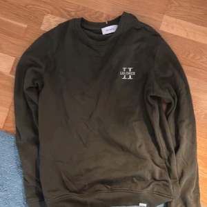 Olivgrön sweatshirt från Les Deux - Snygg olivgrön sweatshirt från Les Deux med broderad vit logga på bröstet. Tröjan har rund hals, långa ärmar och ribbade muddar. Perfekt för dig som gillar stilren och enkel design med en touch av streetwear.