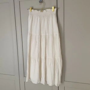 Vit ankellång kjol & Other Stories - Supersöt vit lång kjol från & Other Stories med smockad midja och volanger. Kjolen är tillverkad i 100% viskos och har en luftig, flowy känsla som är perfekt för varma dagar. Passar dig som gillar en chill och feminin stil.