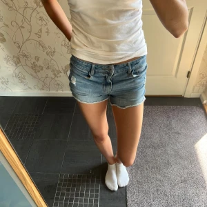 Blå jeansshorts från LAB Industries - Snygga blå jeansshorts från LAB Industries med fransad kant och klassisk femficksdesign. Modellen är lågmidjad och har slitna detaljer framtill för en cool look. Perfekta för varma dagar och passar dig som gillar avslappnad stil.