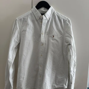Vit skjorta Ralph Lauren XL (18-20) herrstorlek XS - Säljer nu denna klassiska vita skjorta från Ralph Lauren i bomull med broderad logga på bröstet. Den har inga synliga defekter därav i mycket bra skick. Nypris 1300kr, jag säljer för 450kr. Storleken är i XL barn storlek vilket i herrstorlek motsvarar XS eller slim fit S.