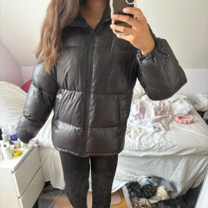 Svart pufferjacka från H&M - Säljer en svart pufferjacka från H&M i storlek XS. Jackan har huva, dragkedja framtill och stora, quiltade partier som ger en riktigt fluffig look. Perfekt för kalla dagar när du vill vara både varm och stilren. Väldigt stor i storleken