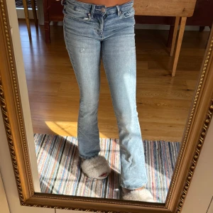 Ljusblå bootcut jeans med slitningar - Säljer ett par ljusblå vero moda jeans med bootcut passform och låg midja, även slitningar. Jeansen har klassiska fem fickor, dragkedja och knapp framtill. Tillverkade i mjukt denimtyg som sitter snyggt och bekvämt. Perfekta för en avslappnad och trendig look.