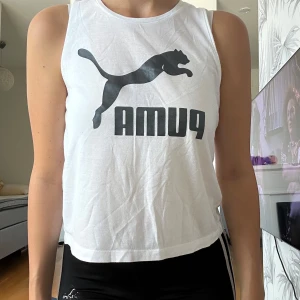 Vit omlott linnetopp från Puma - Säljer en vit ärmlös linnetopp från Puma med svart logga framtill. Toppen har en croppad passform och cool omlottdetalj i ryggen som ger en öppen rygg. Perfekt för träning eller chill dagar när du vill ha något luftigt och sportigt. 152 11-12 år - jag har storlek S