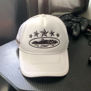 Corteiz keps - Säljer en vit truckerkeps från Corteiz med svart broderad logga och stjärnor framtill och på sidorna. Kepsen har mesh-bakstycke för extra ventilation och justerbar passform. Perfekt för dig som vill sticka ut med en clean och modern look. Skriv innan köp, pris kan diskuteras