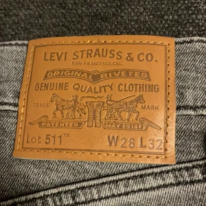 Levi's 511 grå jeans W28 L32 - Säljer ett par grå Levi's 511 jeans med klassisk femficksdesign och snyggt tvättad finish. Jeansen har smal passform och är tillverkade i slitstarkt denim med den ikoniska läderpatchen bak. Perfekta för dig som gillar en clean och stilren look.