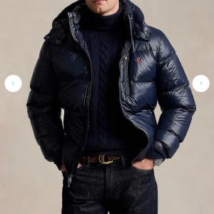 Mörkblå dunjacka från Polo Ralph Lauren - Snygg mörkblå dunjacka från Polo Ralph Lauren med klassisk pufferstil. Jackan har huva, dragkedja framtill och flera fickor, inklusive en bröstficka med dragkedja. Ikoniska röda Polo-loggan på bröstet. Perfekt för kalla dagar och riktigt skön att bära. Köpte jackan 2024 och säljer pågrund av att det är herr model. Pris kan diskuteras. Skriv för bilder på