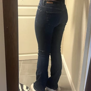 Mörkblå bootcut jeans - Snygga mörkblå jeans med bootcut passform och klassisk femficksdesign. Jeansen har medel midja och är tillverkade i stretchigt denim som sitter tajt över låren och släpper ut vid vaden. Perfekta för dig som gillar en tidlös och trendig look. Jeansen är från b.young helt oanvända