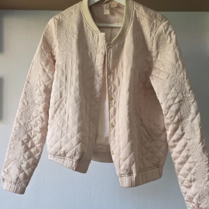 Quiltad bomberjacka från H&M Divided - Säljer en ljusbeige quiltad bomberjacka från H&M Divided i storlek 38. Jackan har snygga broderade detaljer, guldiga tryckknappar och ribbade muddar. Den är sååå fin men tyvärr för liten för mig. Fickor på sidorna och lätt fodrad! Passar perfekt till sensommar och höst 🌟