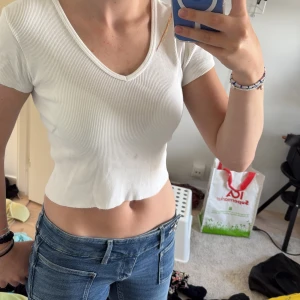 Vit ribbad croppad topp Brandy Melville - Säljer en vit croppad topp från Brandy Melville. Toppen är ribbad med v-ringning och korta ärmar. Skriv om ni har frågor🥰💕