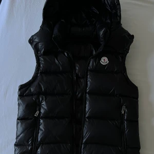 Moncler väst  - Säljer min Moncler-väst som jag tyvärr har växt ur. Västen är i gott skick, vilket ni kan se på bilderna. Kvittot medföljer tyvärr inte!! Har ni några frågor eller prisförslag är det bara att slänga iväg ett meddelande! Endast seriösa köpare. Priset är inte hugget i sten 🪨😉