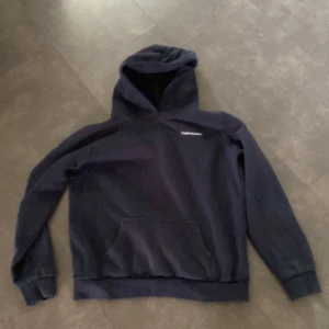 Mörkblå hoodie från Peak Performance - Säljer en mörkblå hoodie från Peak Performance med klassisk logga på bröstet. Tröjan har huva, magficka och ribbade muddar. Perfekt för dig som gillar en enkel och stilren look. Materialet är mjuk bomull som känns skönt mot huden.