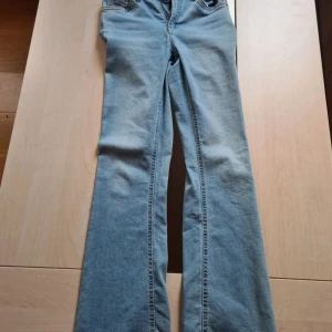 Ljusblå bootcut jeans - Snygga ljusblå jeans från Denim Day i storlek 164. Modellen har bootcut-ben, klassisk femficksdesign och justerbar resår i midjan. Tillverkade i mjukt denimtyg med dragkedja och knapp framtill. Perfekta för dig som gillar retrovibbar och bekväm passform. Midjan är inte hög men inte heller låg (någonstans mittemellan). Har dock en lite fläck vid baksida ben som kah kan skicka bild på privat