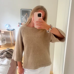 Beige stickad tröja med trekvartsärm - Mysig beige stickad tröja med rund halsringning och trekvartsärmar. Tröjan har en loose passform och är perfekt för lager-på-lager. Enkel och stilren design som funkar till många olika outfits.