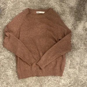 Brun stickad tröja från ONLY  - Mysig brun/gammal dags rosa stickad tröja från ONLY i storlek XS. Tröjan har rund halsringning, långa ärmar och ribbade muddar vid ärmslut och nederkant. 