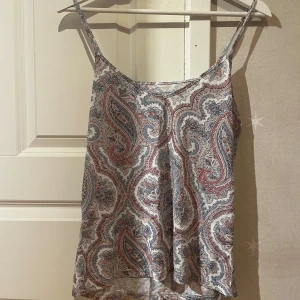 Paisleymönstrad linnetopp från BikBok - Paisleymönstrad linnetopp från BikBok i vitt, blått och rosa. Tunt och luftigt material med smala axelband och rak passform. Perfekt för varma dagar och enkel att styla med jeans eller kjol.