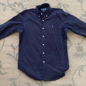 Mörkblå skjorta från Ralph Lauren - Klassisk mörkblå skjorta från Ralph Lauren i bomull med broderad lila logga på bröstet. Nypris 1800kr