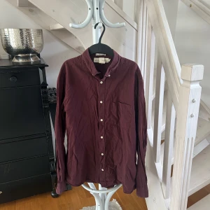 Vinröd skjorta med knappar - Vinröd skjorta från h&m Man med klassisk krage, vita knappar och bröstficka. Skjortan är långärmad och har en rak passform. Perfekt för dig som gillar stilrena plagg med enkel design.