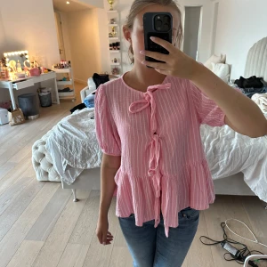 Rosa randig blus med knyt  - Supersöt rosa blus från Kilky med vita ränder och volang nertill. Blusen har korta puffärmar och knyt framtill som ger en gullig touch. Materialet känns lätt och skönt mot huden. Aldrig använd, köpte av en väns mamma som säljer kläder därför är det ingen prislapp. 