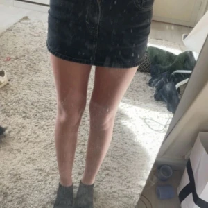 Svart jeanskjol från Lindex - Snygg svart jeanskjol från Lindex med klassisk femficksdesign och synliga sömmar. Kjolen är kort och har knapp och dragkedja framtill. Perfekt att matcha med sneakers eller boots för en cool look.