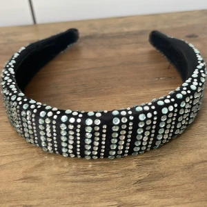 Svart diadem med glittriga stenar - Snyggt svart diadem täckt av glittrande silverfärgade stenar i rader. Bred modell som ger ett statement till din look och passar perfekt när du vill sticka ut. Diademet har en lyxig känsla och är bekvämt att bära hela dagen.