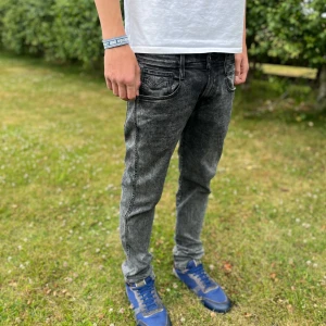 Replay Hyperflex Anbass grå svarta jeans - Säljer ett par Replay Hyperflex Anbass jeans i tvättad grå svart färg. Slim fit-modell med klassiska fem fickor och snygga detaljer på bakfickorna. Jeansen är stretchiga och sitter riktigt skönt. Perfekta för dig som gillar en modern och stilren look. Fråga mig om du har frågor🙌