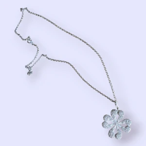 Halsband från Thomas Sabo - Snyggt halsband i sterling silver 925 med ett stort, detaljerat hänge i form av en blomma/fyrklöver med vita stenar. Kedjan är tunn och klassisk, perfekt för att ge din outfit en cool touch.