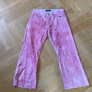Rosa bootcut jeans från Indian Rags - Unika rosa jeans från Indian Rags med cool batikmönster och bootcut-ben. Byxorna har klassisk femficksdesign, råa kanter nertill och är gjorda i mjuk bomull. Perfekta för dig som vill sticka ut med färg och retrovibe.
