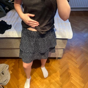  volangkjol med vita prickar - Supersöt mörkblå kortkjol med vita prickar och dubbla volanger. Kjolen har resår i midjan. 