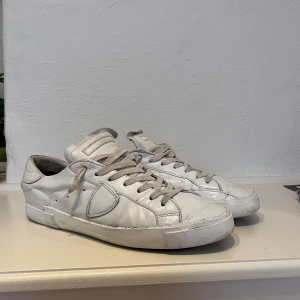 Vita Philippe Model - Stilrena vita sneakers i skinn med klassisk låg profil och rund tå. Skorna har vita snören och en vit sula med svart undersida. Perfekta för dig som gillar en clean och enkel look till vardags.