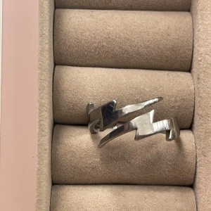 Cool silverring med blixtdesign - Säljer en unik silverfärgad ring med blixtformad design. Ringen har en öppen justerbar form och glänsande yta som ger en edgy och modern vibe. Perfekt för dig som vill sticka ut med dina accessoarer.