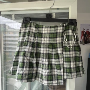 Grön rutig skort, The Ragged Priest - Grön och vit rutig kort skort (kjol+skjorts) från The Ragged Priest i omlottmodell med cool silverfärgad kedjedetalj. Kjolen har plisserad look och är tillverkad i ett lätt bomullstyg. Perfekt för dig som vill sticka ut med en edgy vibe. Aldrig använd pga fel storlek. 